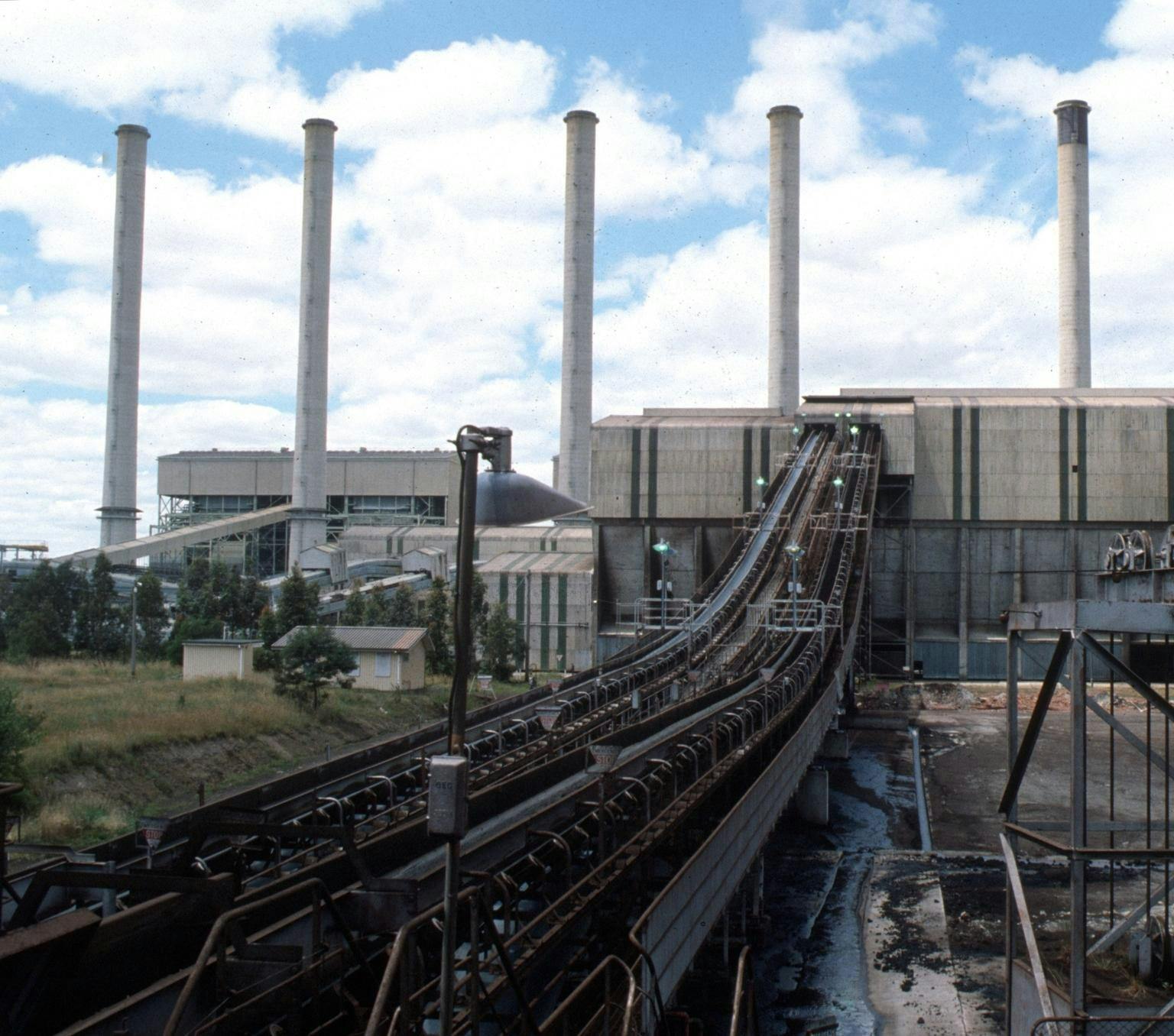 four chimneys rising a grey building with a coal transporting belt leading into the building