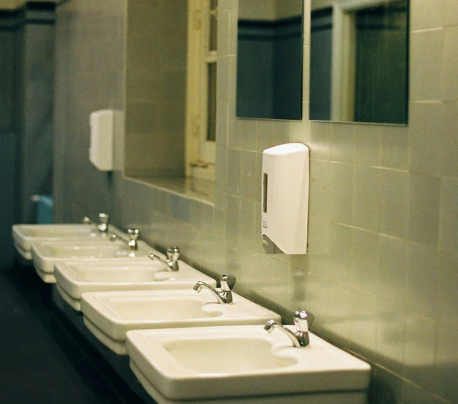 Row of sinks in a public restroom. There are mirrors and hand soap dispensers above the sinks