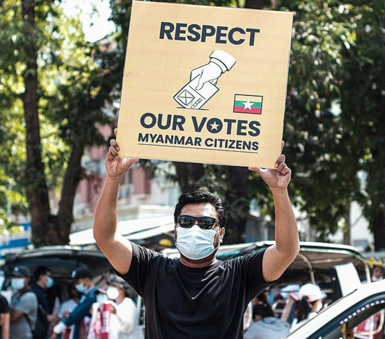 Man holding a protest sign reading: 'Respect our votes, Myanmar citizens.'