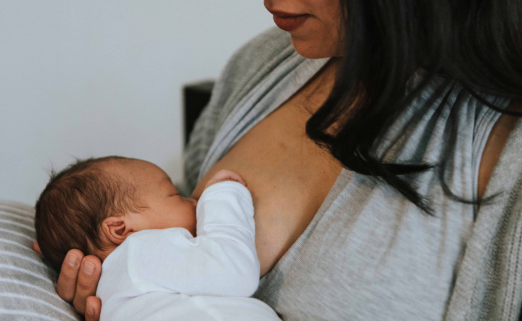 A woman holds her baby to her breast, cradling the back of their head with her hand.