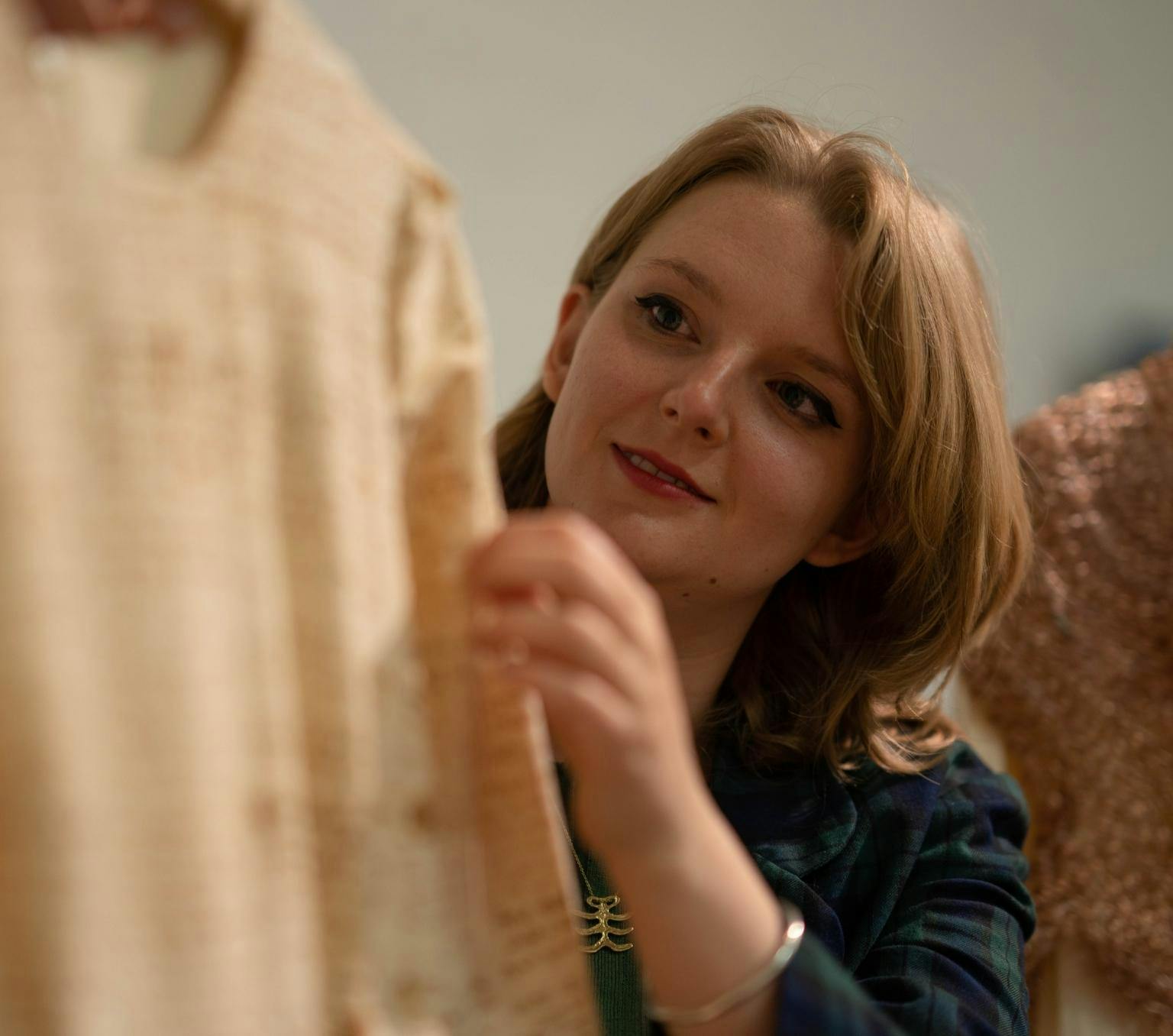 Saskia Morris looks closely at a cream dress, which is part of her artwork. He hand gently touches the sleeve of the dress.