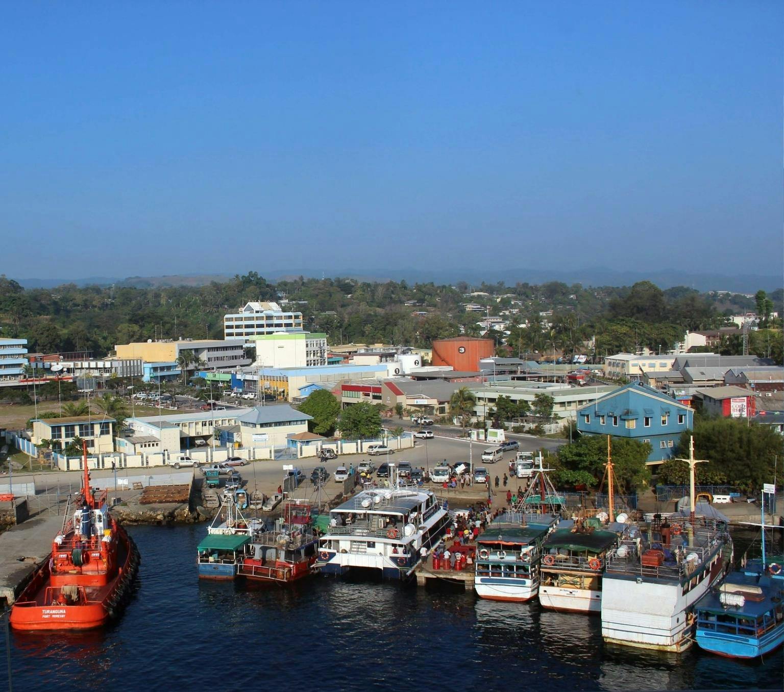 view of a port with various boats docked. Behind are buildings, and a blue sky