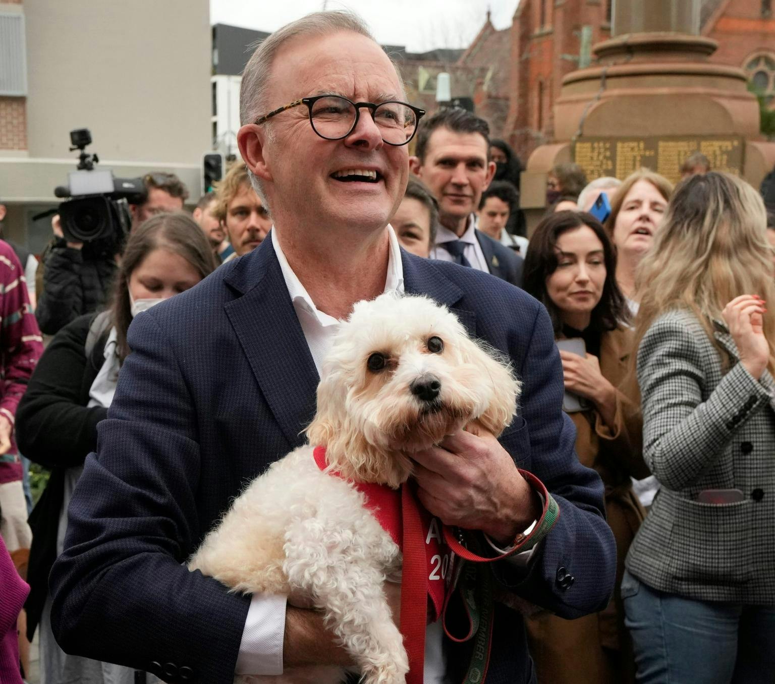 Anthony Albanese holds his small white dog Toto while surrounded by people on the campaign trail.