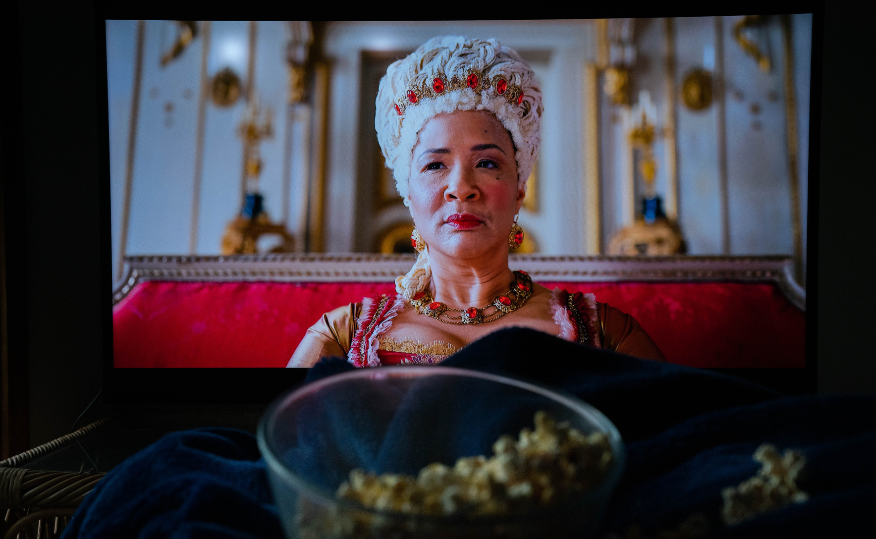 Queen Charlotte from Bridgerton is shown on a TV screen, behind a bowl of popcorn.