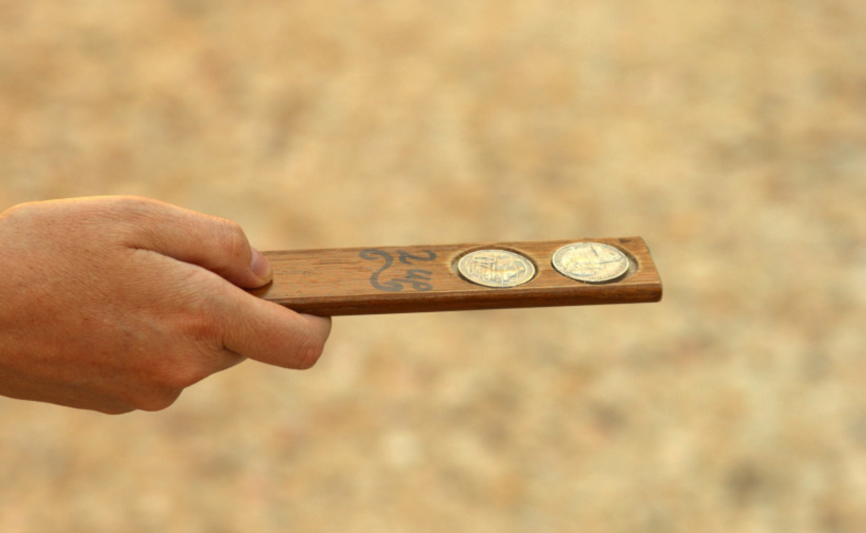 Person's hand holds a two up paddle with two 20 cent coins resting on it.