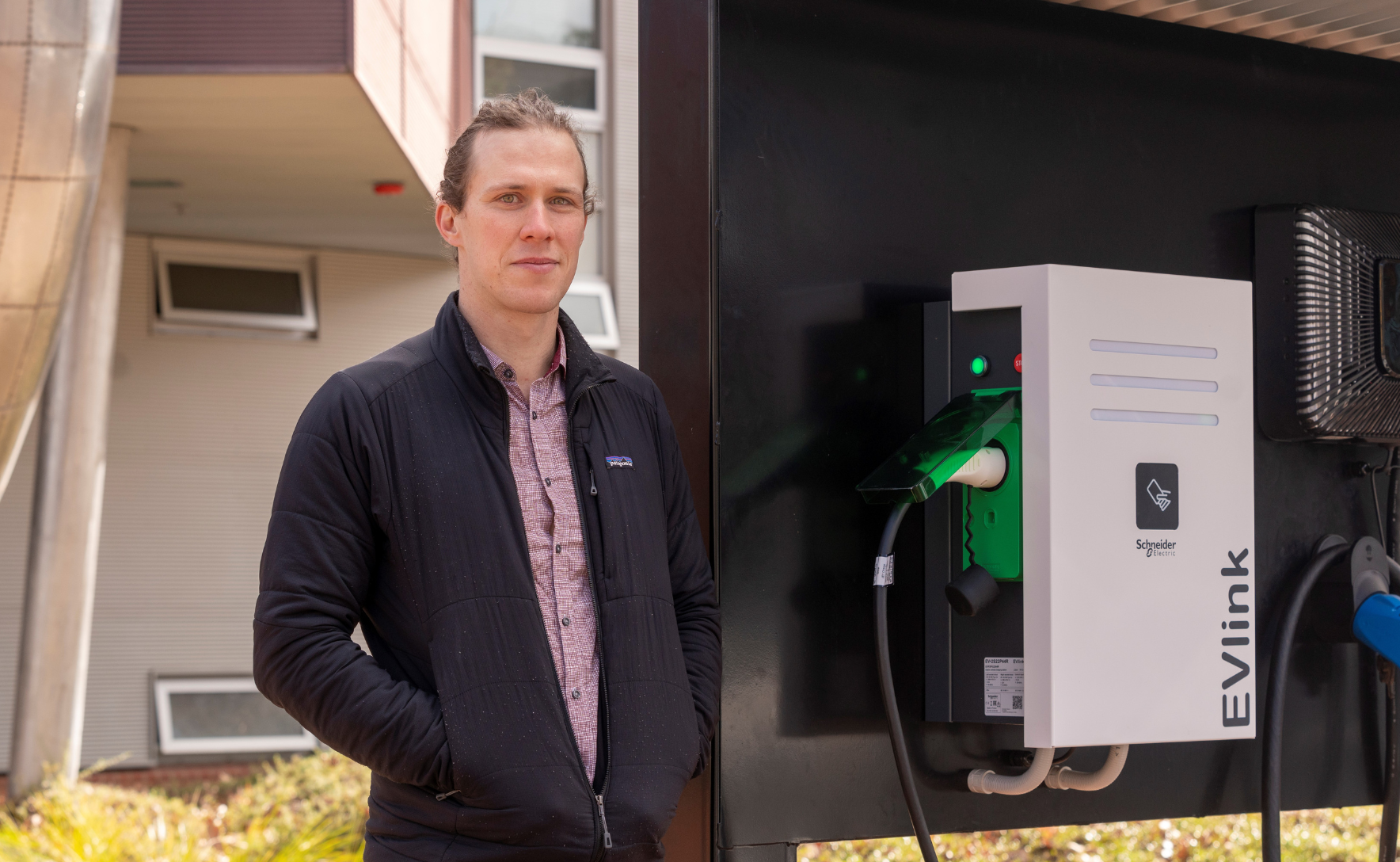 Dr Bjorn Stumberg standing next to an electric vehicle charging station.