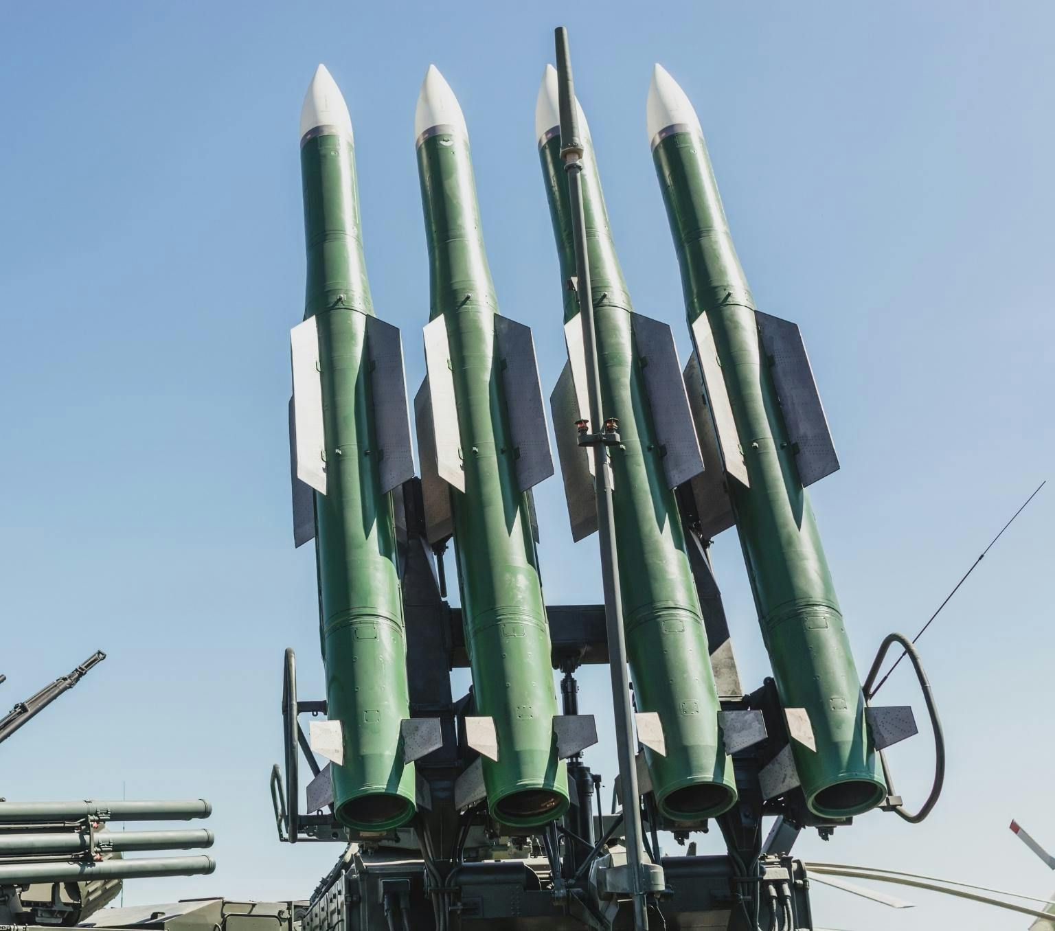 Four large green missiles attached to a launcher point up at a blue sky.