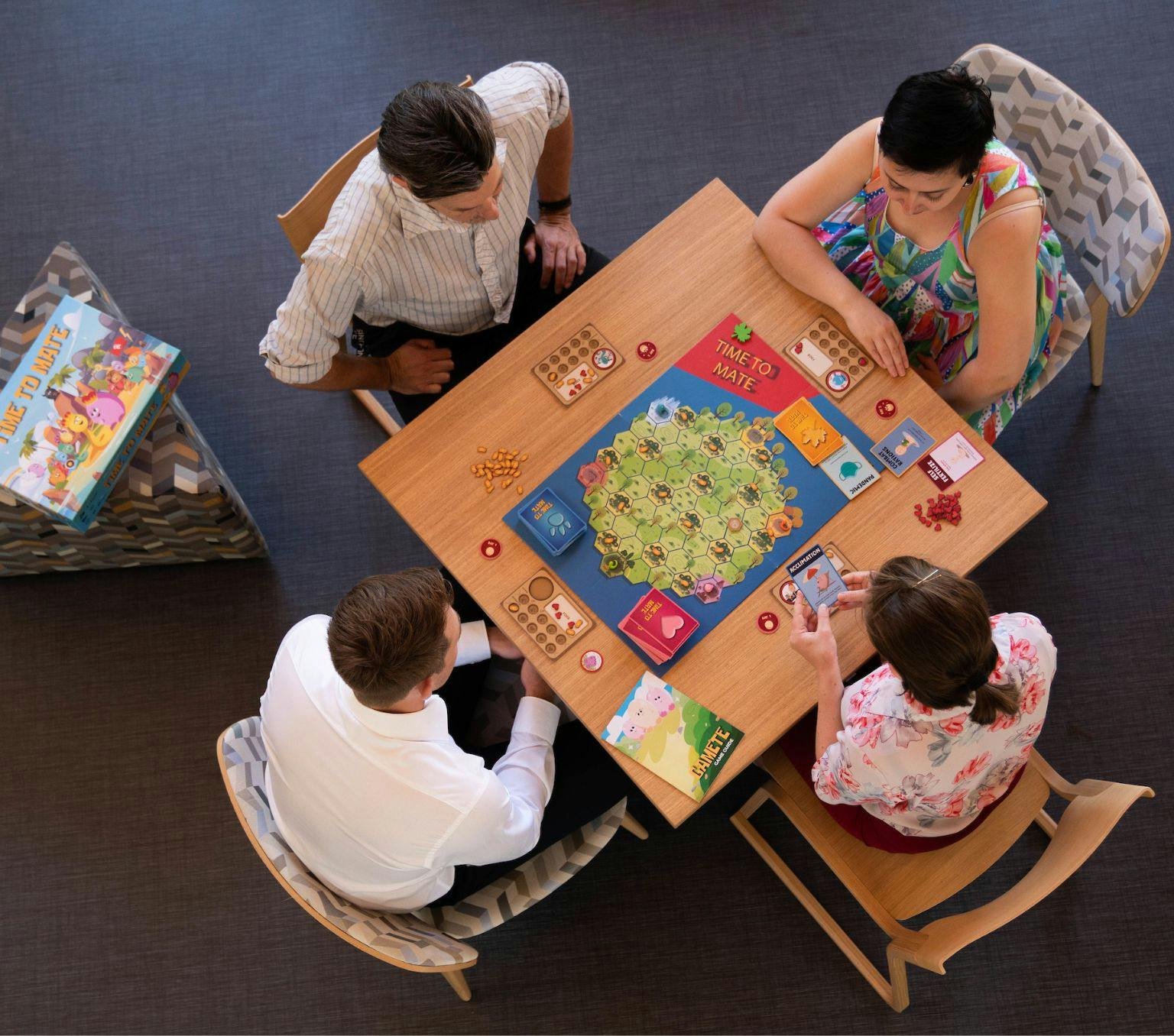 4 people sit around a table playing a board game.