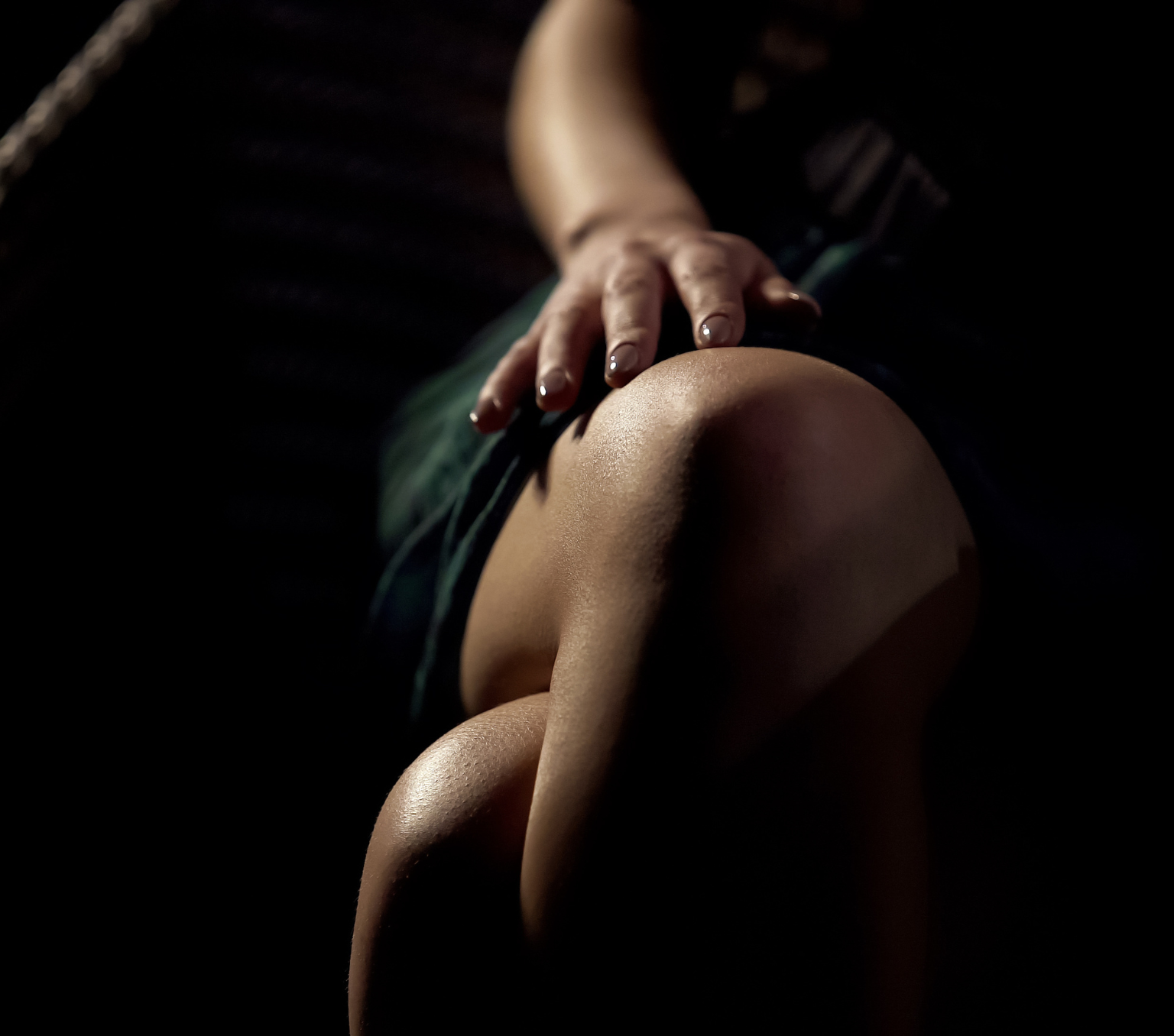 A woman wearing a dress has her legs crossed and her hand on the top of her leg.
