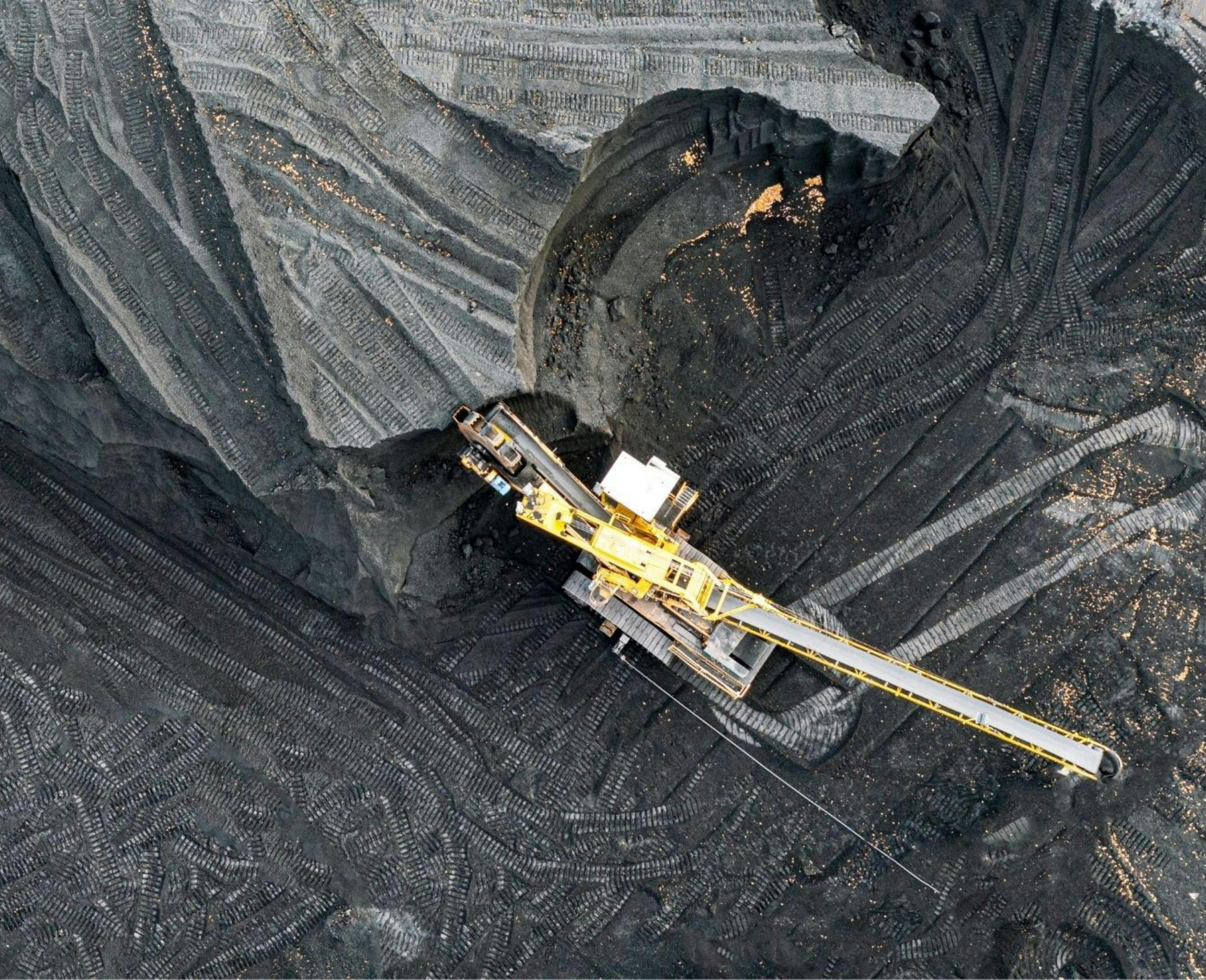 aerial shot of a yellow excavator in a black coal mine