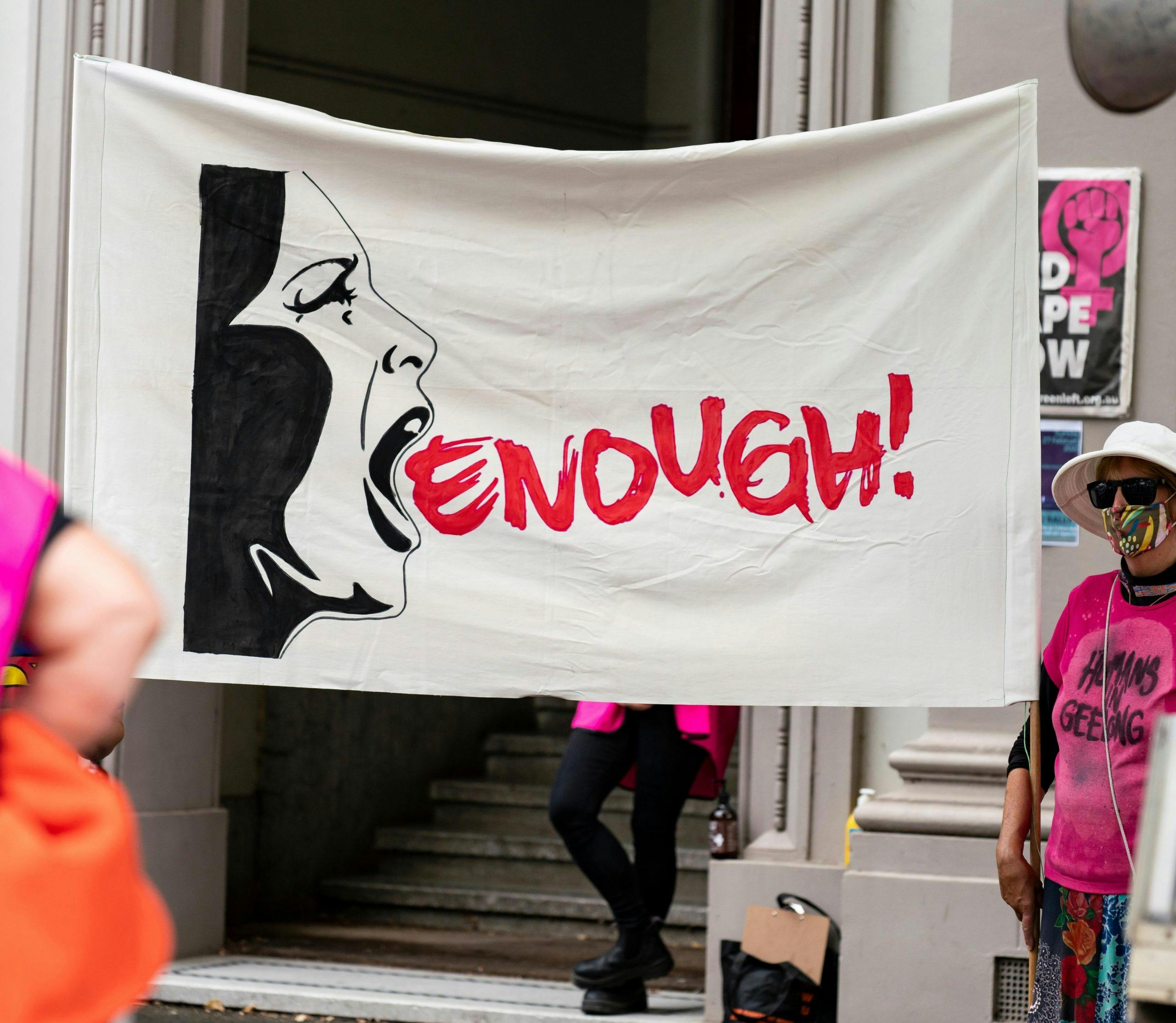 Photo of a banner from a Geelong women's rights protest which reads ENOUGH!.. The text is positioned coming out from a graphic illustration of a woman's profile shouting.