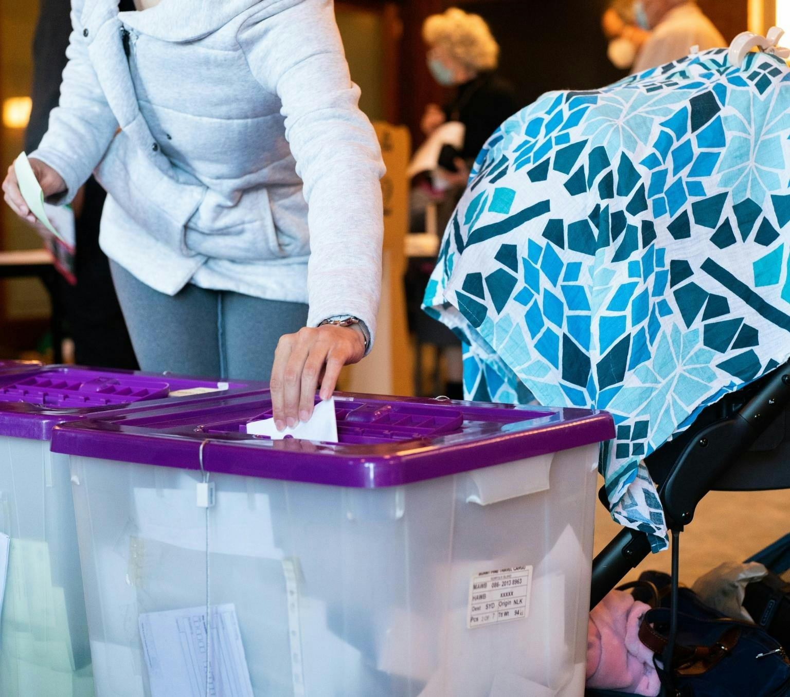 An unidentified female voter casting their vote in a ballot box at the 2022 Australian federal election. There is a baby pram next to the voter.