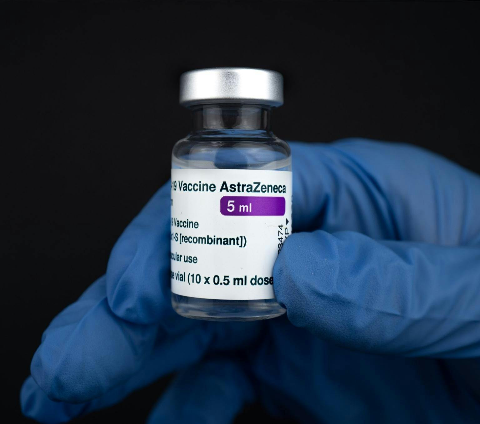 An astraveneca covid vaccine vial is held by a hand wearing blue gloves.