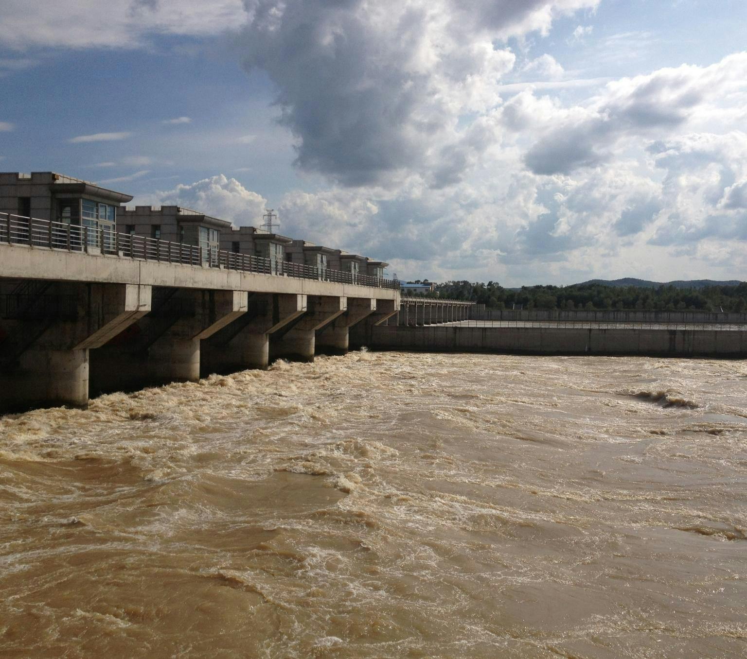 Brown water flows from a concrete dam structure, which runs the width of a river.