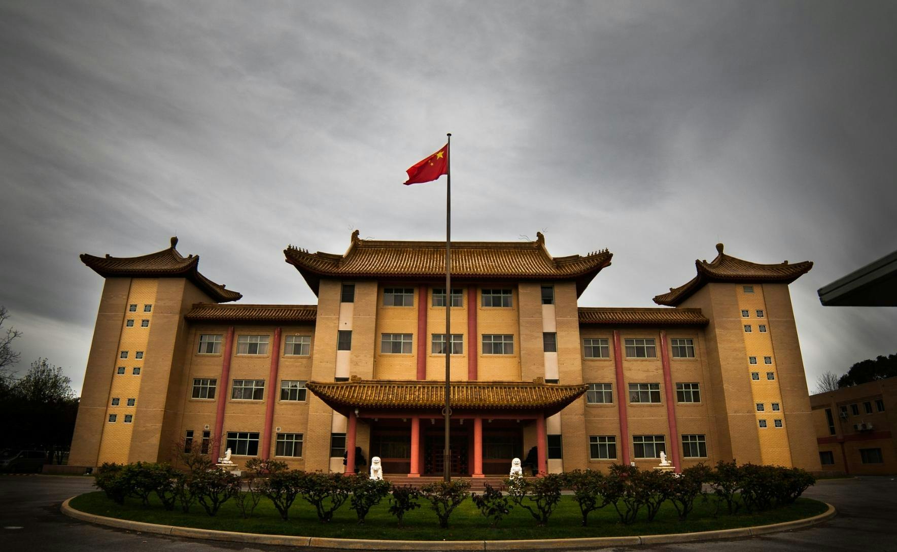 Yellow brick building with red pillars and a red and yellow Chinese flag flying in front.