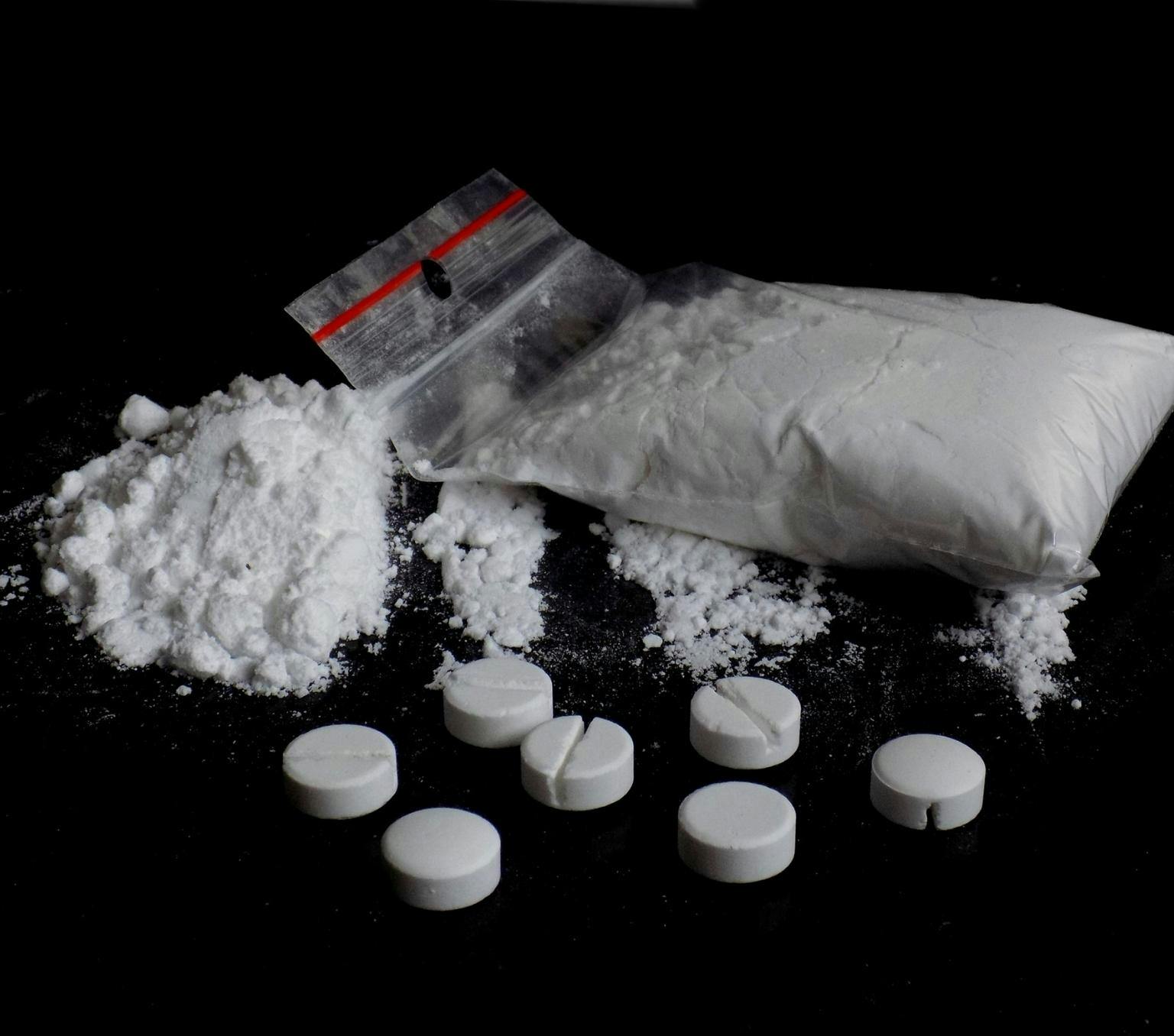 White pills, white powder and a small ziplock bag of white powder on a black background.