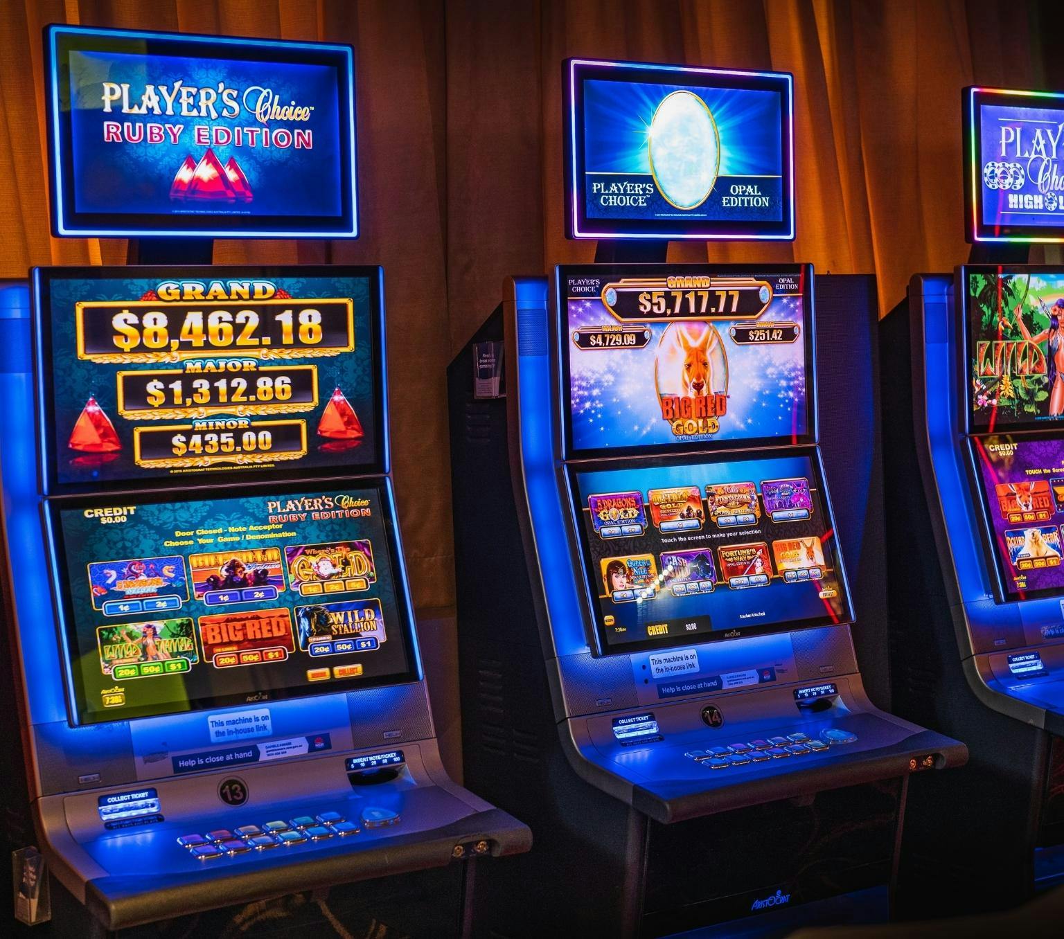 Three bright pokie machines lined up against a dark wall.