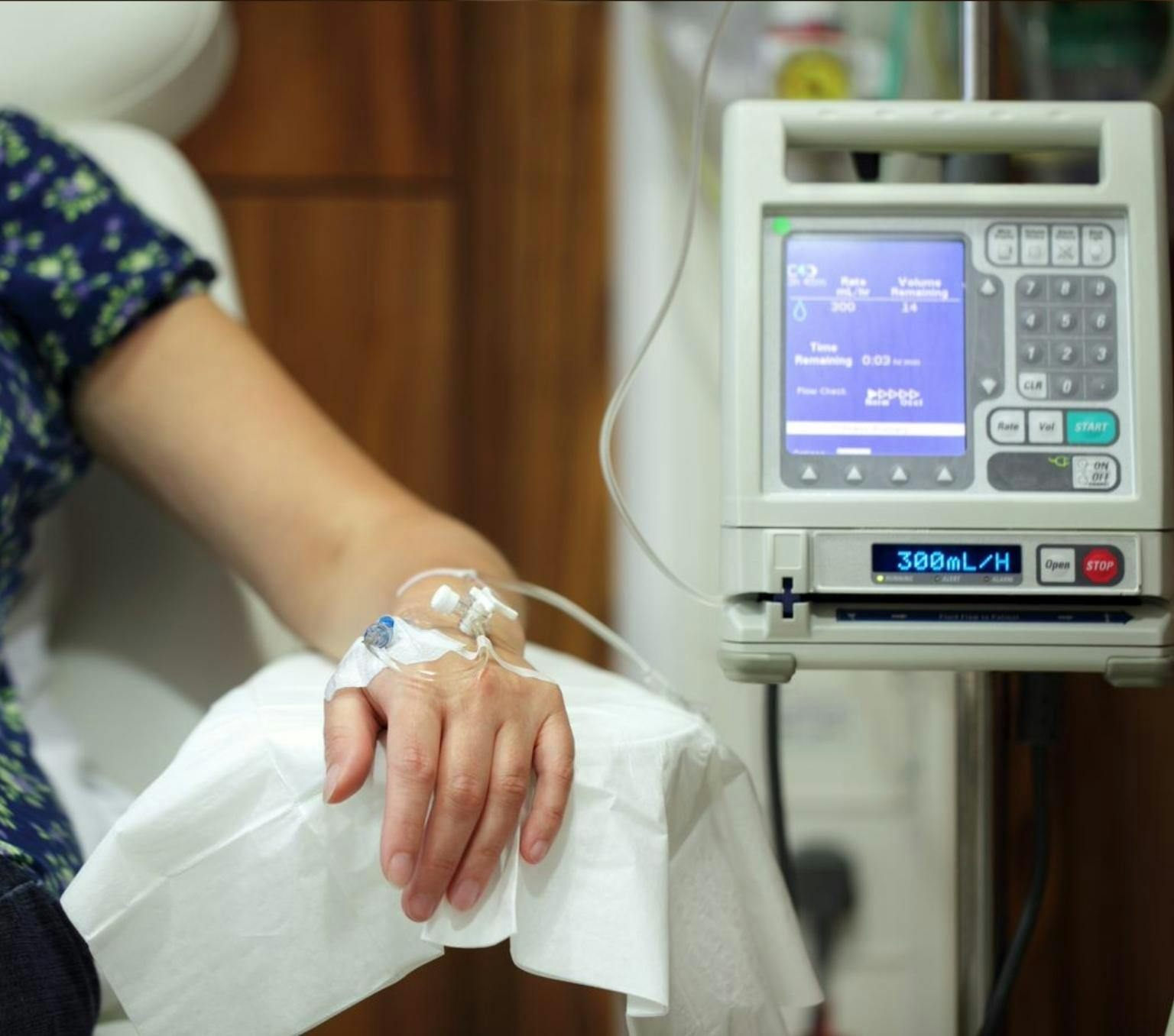 A person's arm with an IV drip and a monitoring machine.