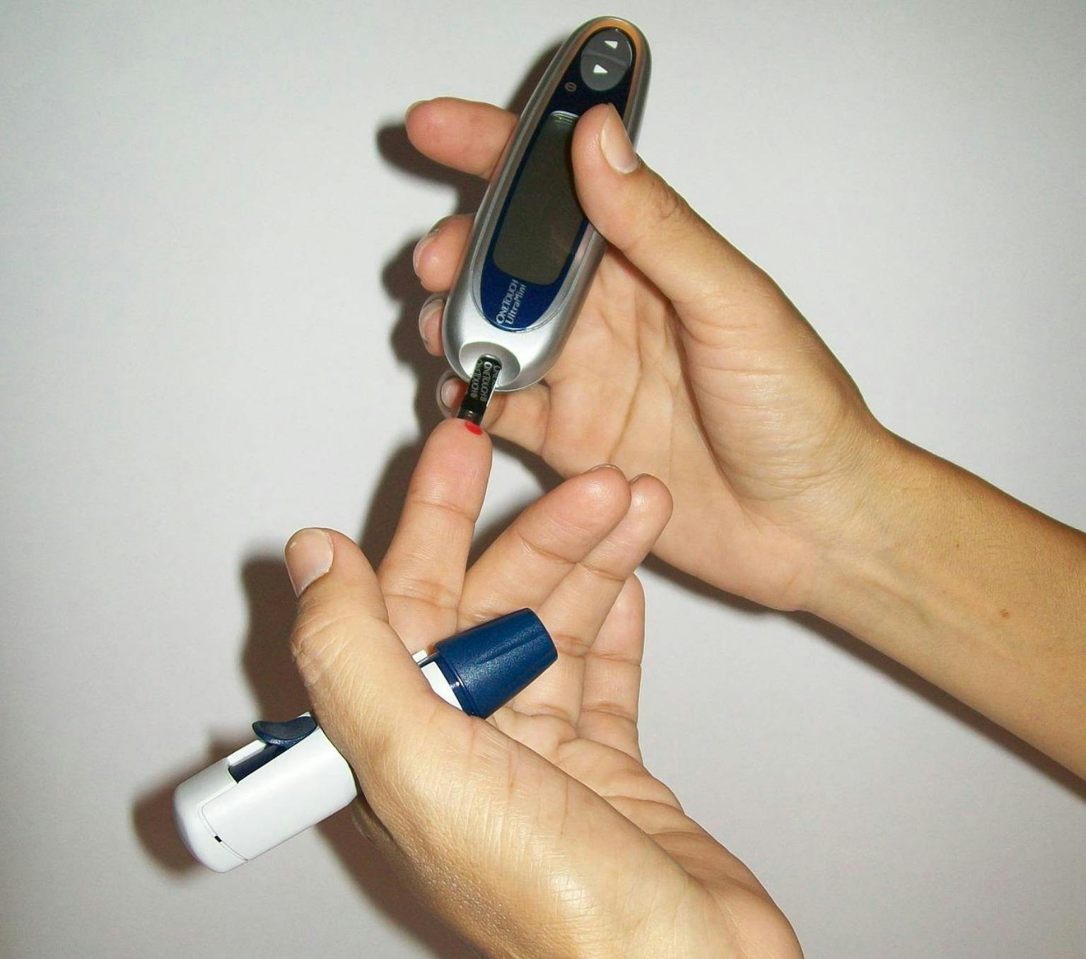 Close up of a person's hands holding a glucose monitor to their index finger to test their blood sugar.