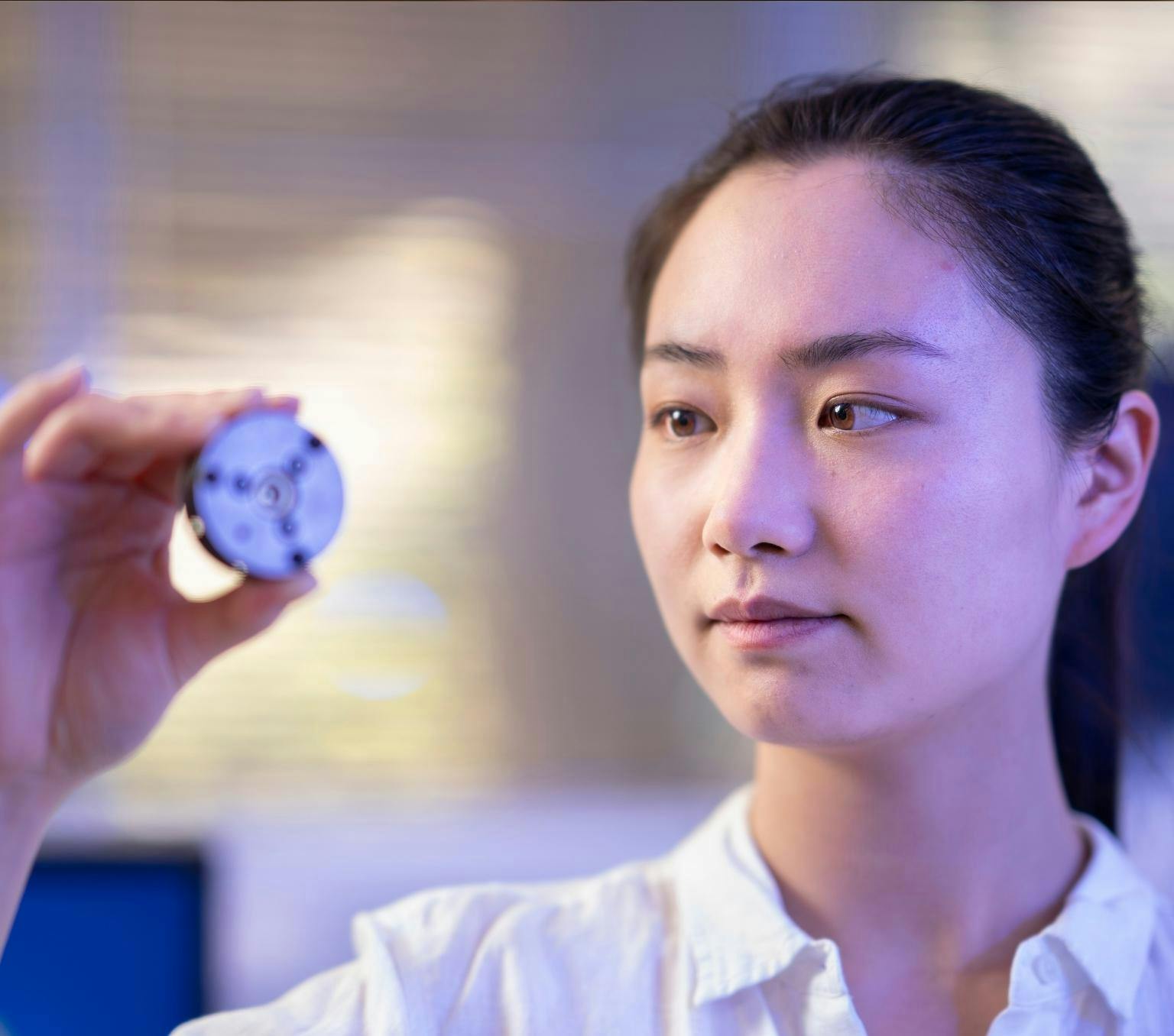 Xingshuo Huang looks at a small metal disc she is holding in her right hand.