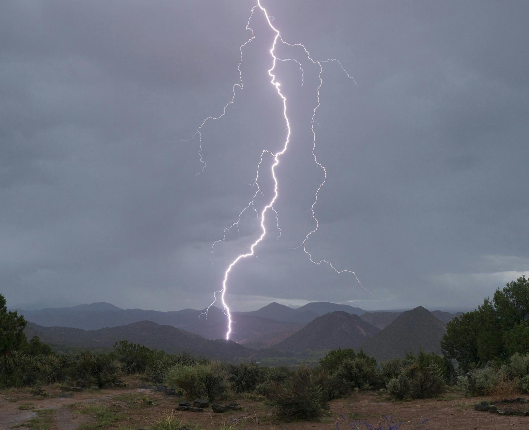 Bolt of lightning reaches from the sky into a mountain range.