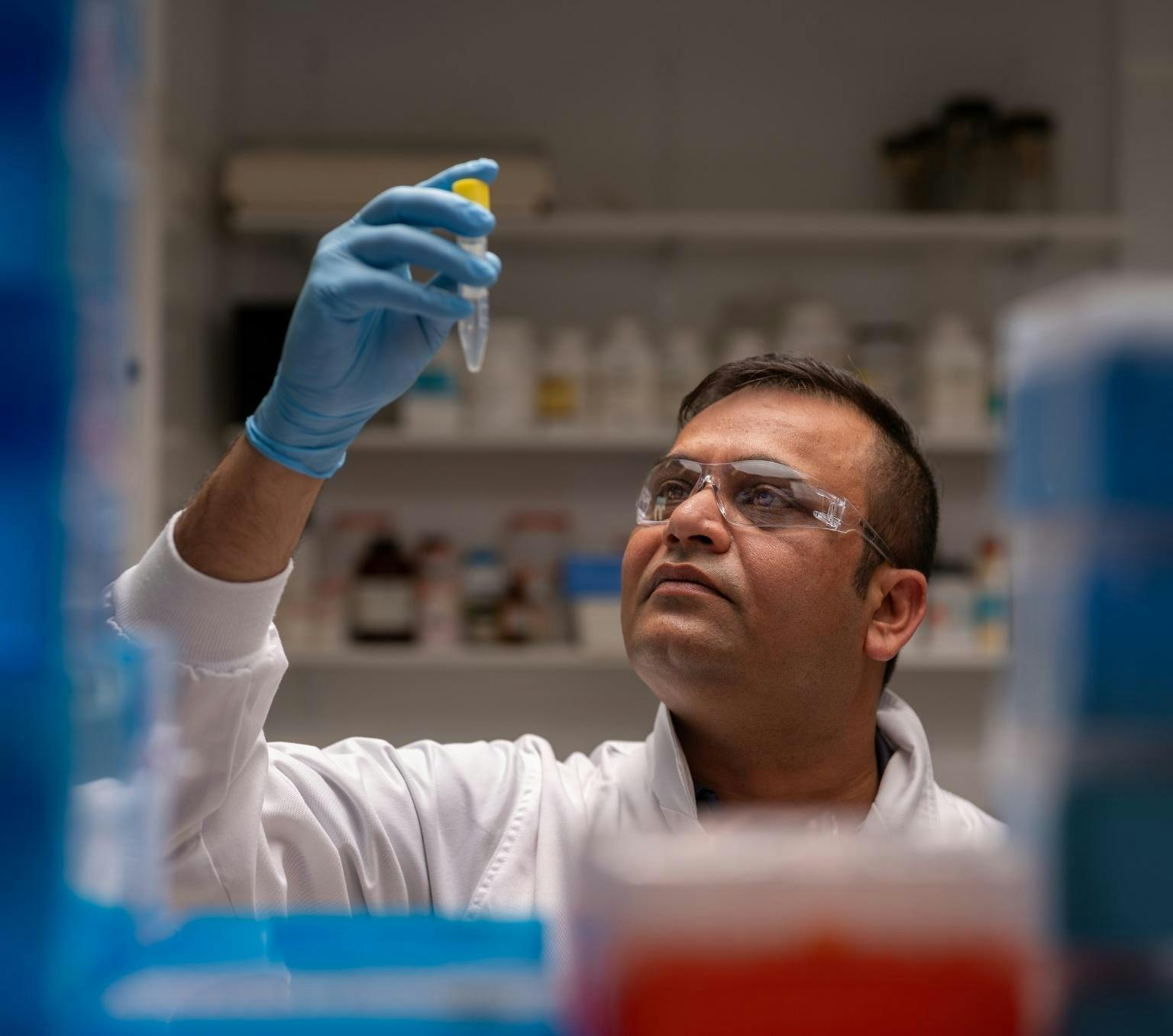 Dr Hardip Patel in a science lab holding up a test tube containing an unknown substance