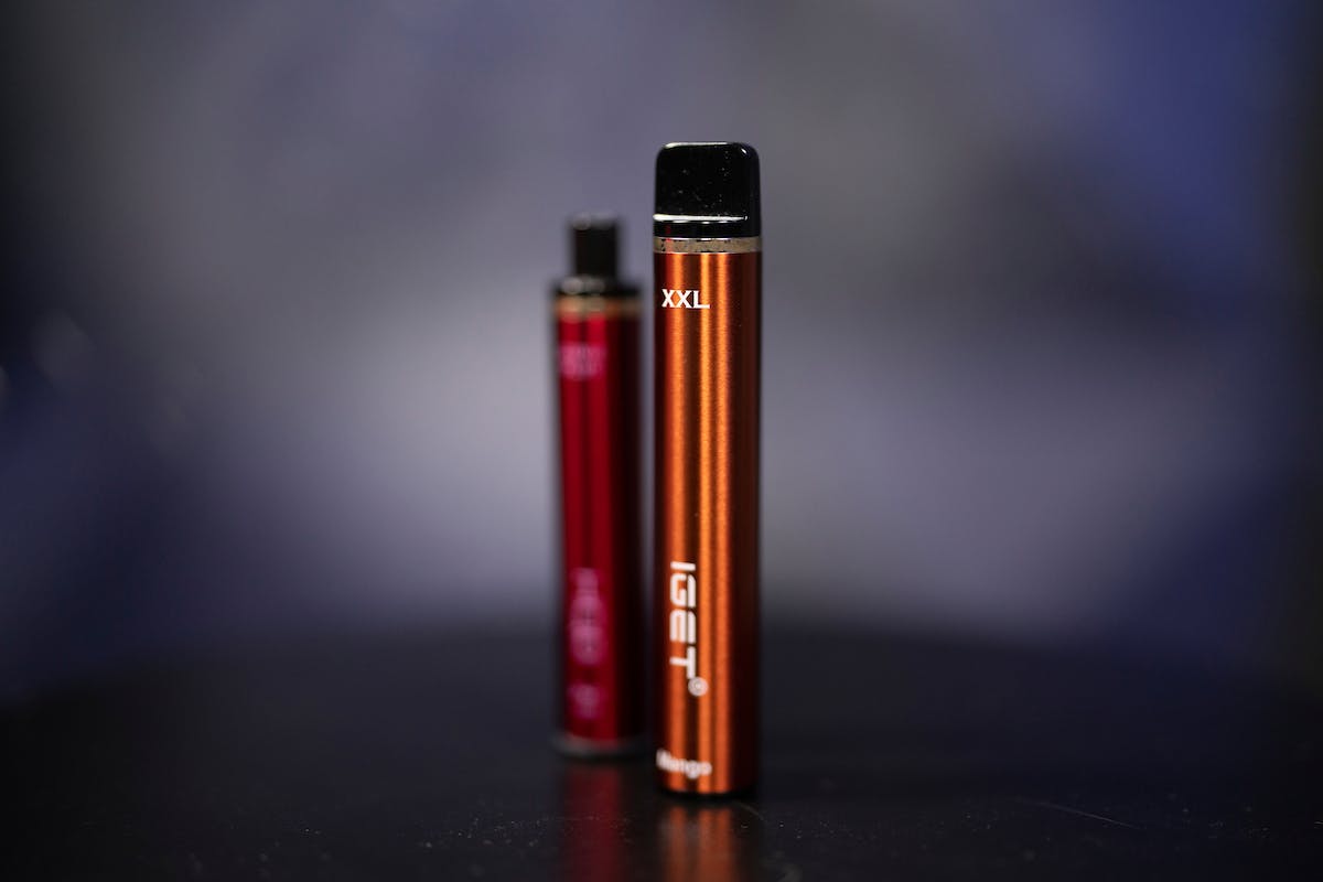 two e-cigarettes are pictured, they are red and orange