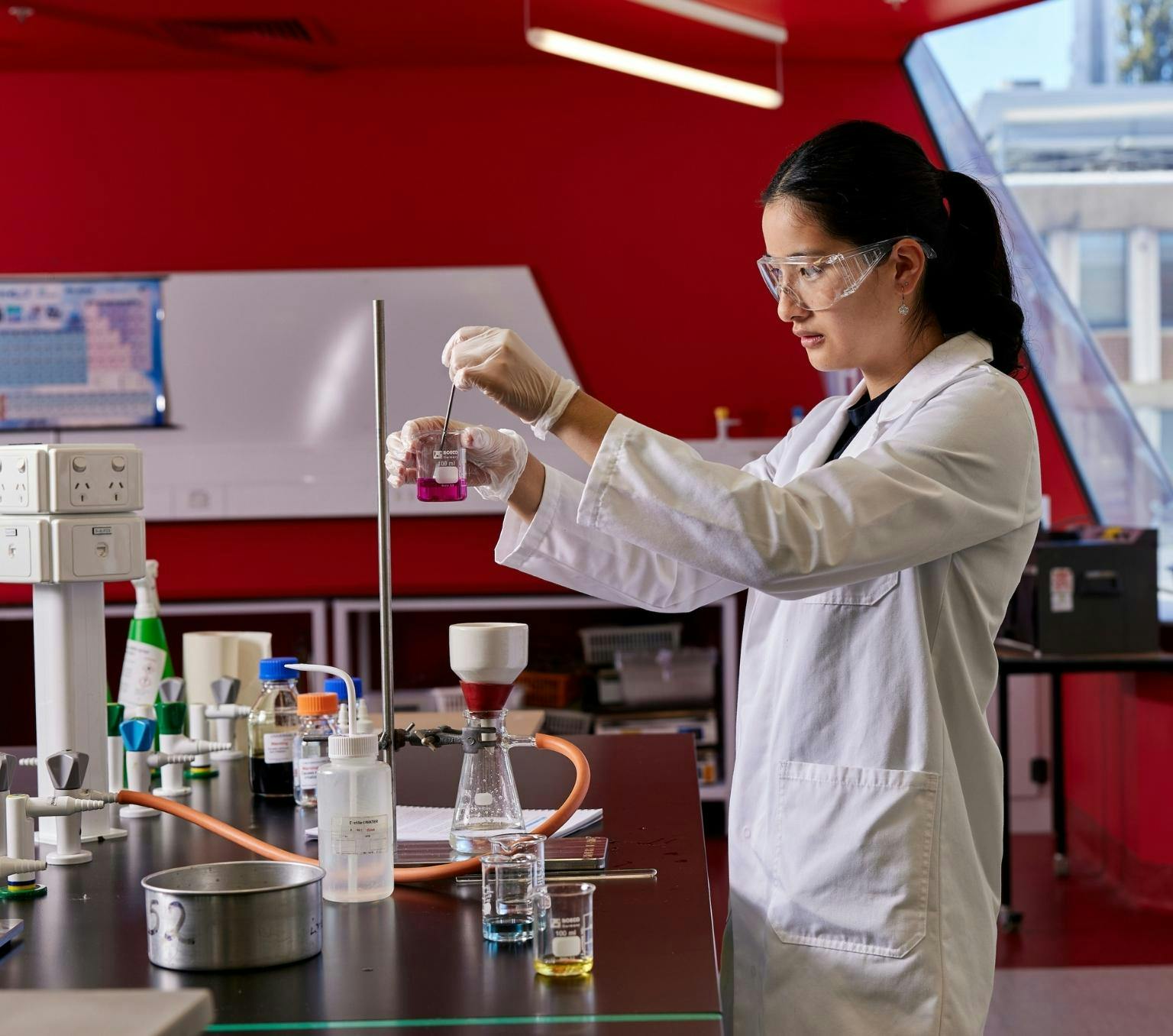 A woman in a white coat holds a beaker in a lab.