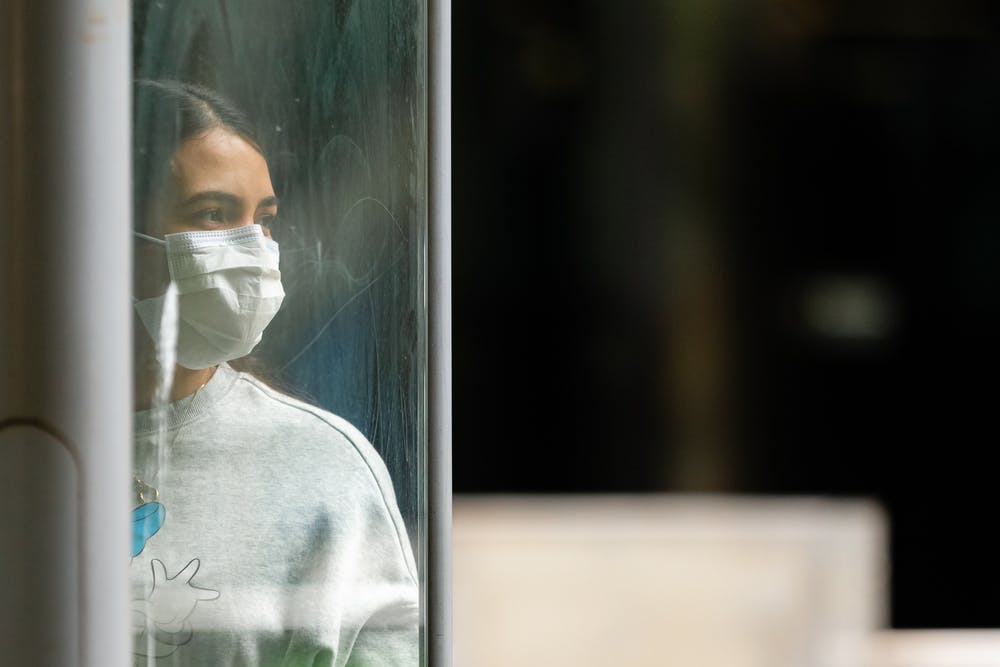 woman is standing behind a glass pane and wearing a mask