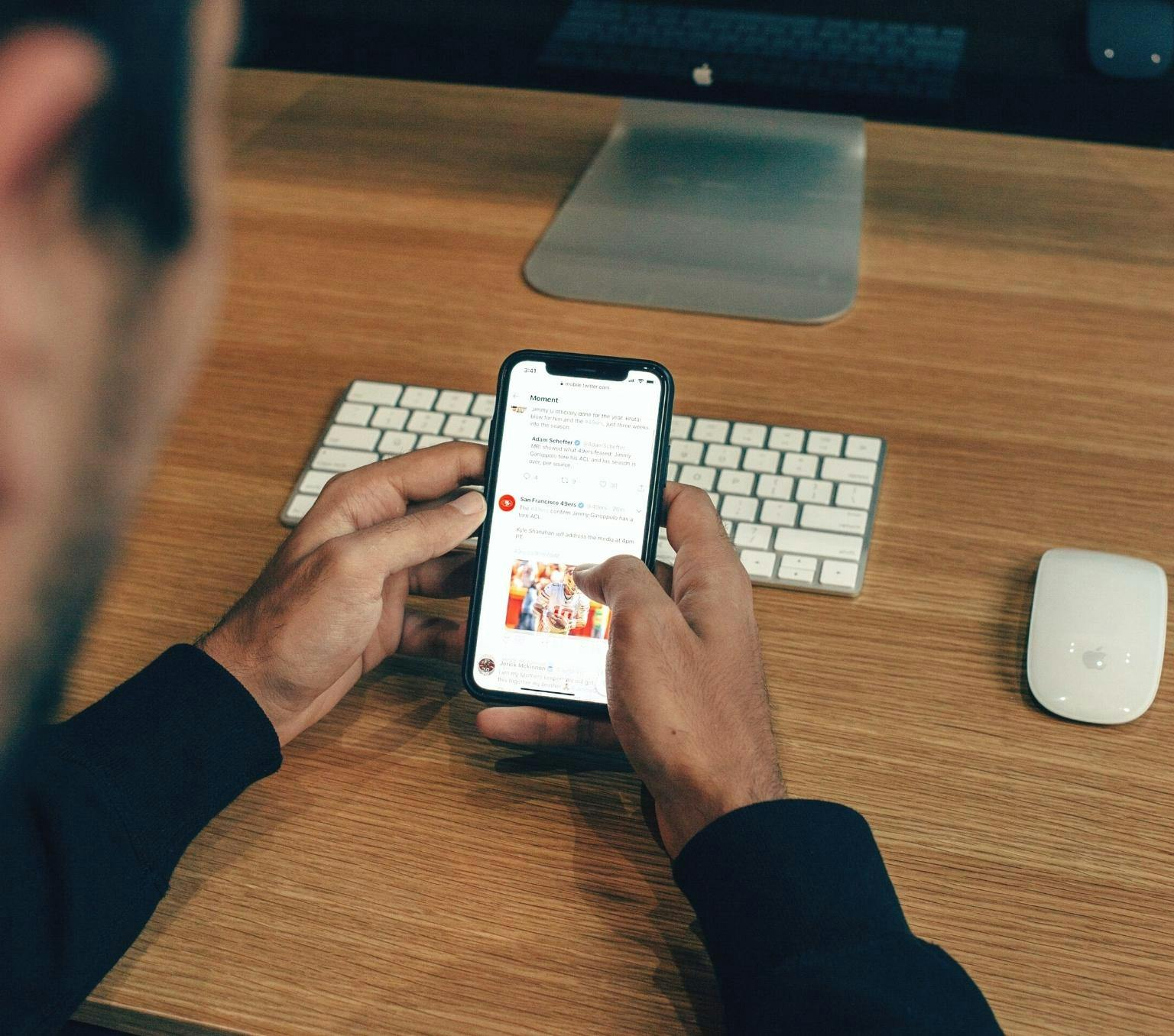 closeup of a man's hands holding an iphone as he scrolls through a social media news feed