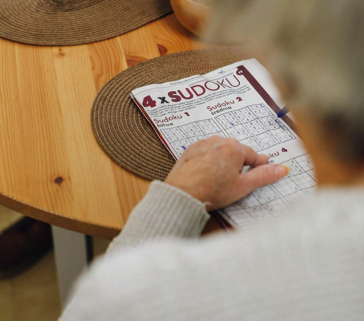 older woman's hands are in view completing a sudoku puzzle