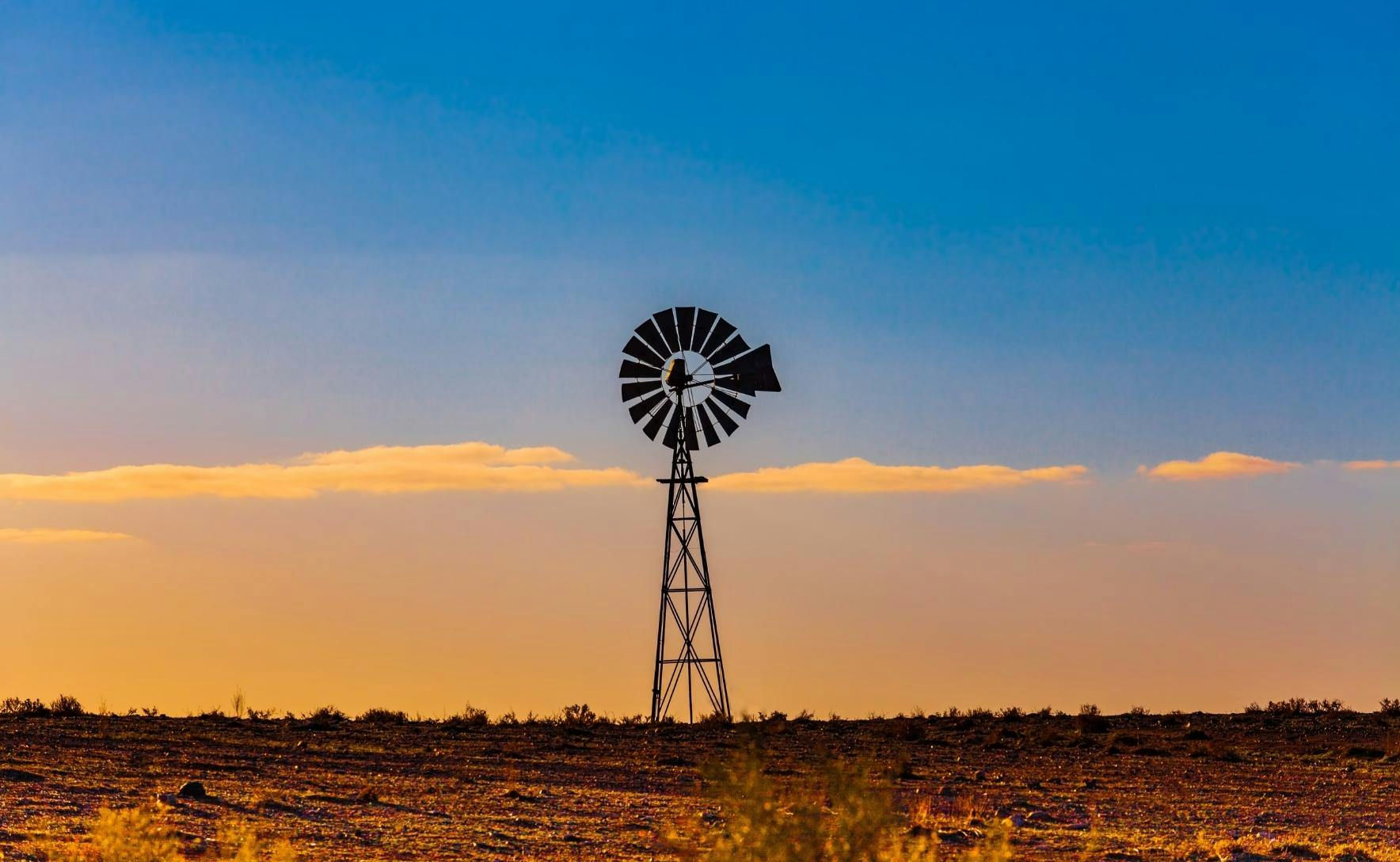 windmill pictured on bare flat country. The sun is setting creating a sky that is blue and orange