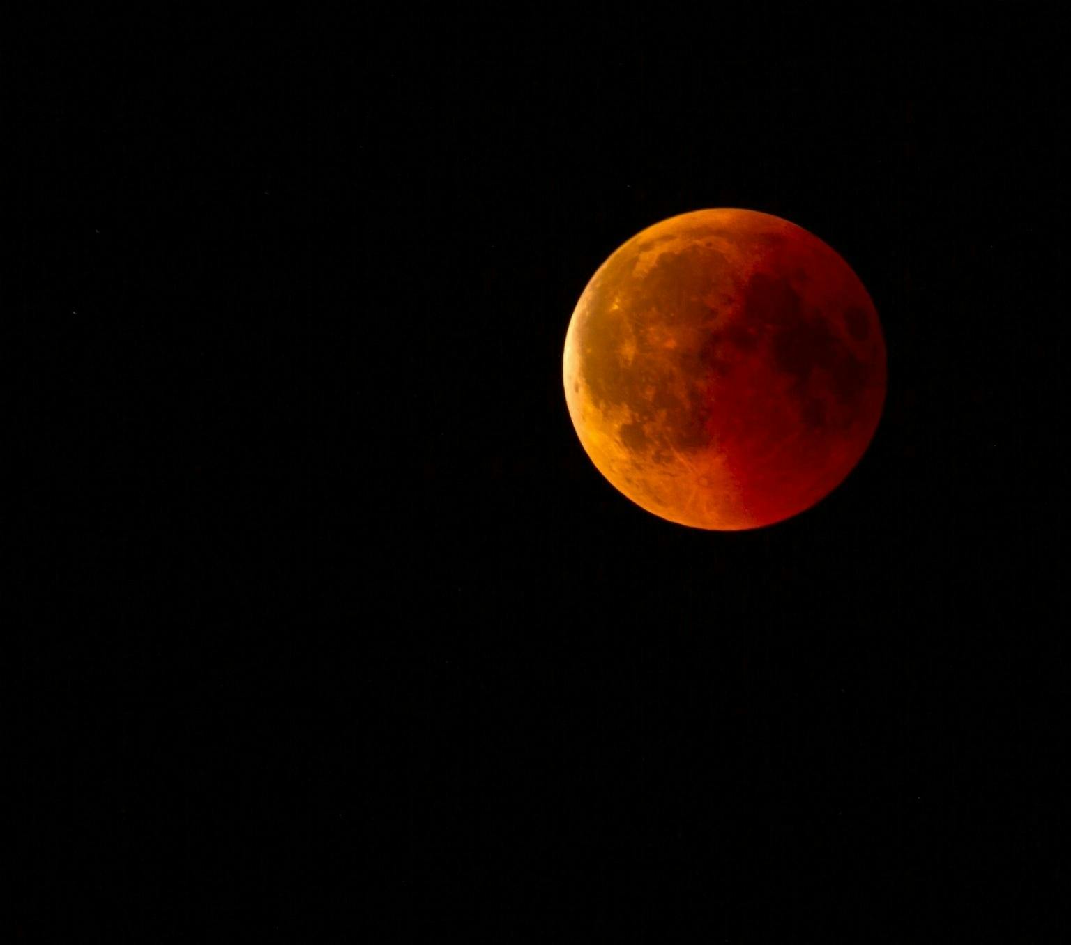 A moon in a red and brownish colour, against a black sky