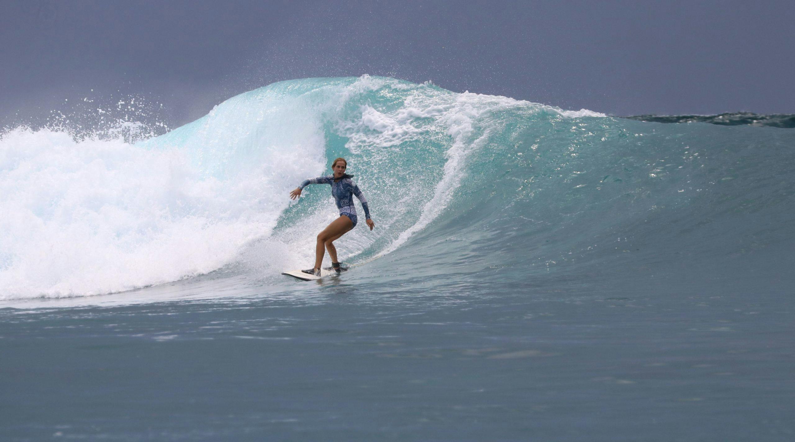 Ana Manero rides a surfboard while a wave breaks behind her.