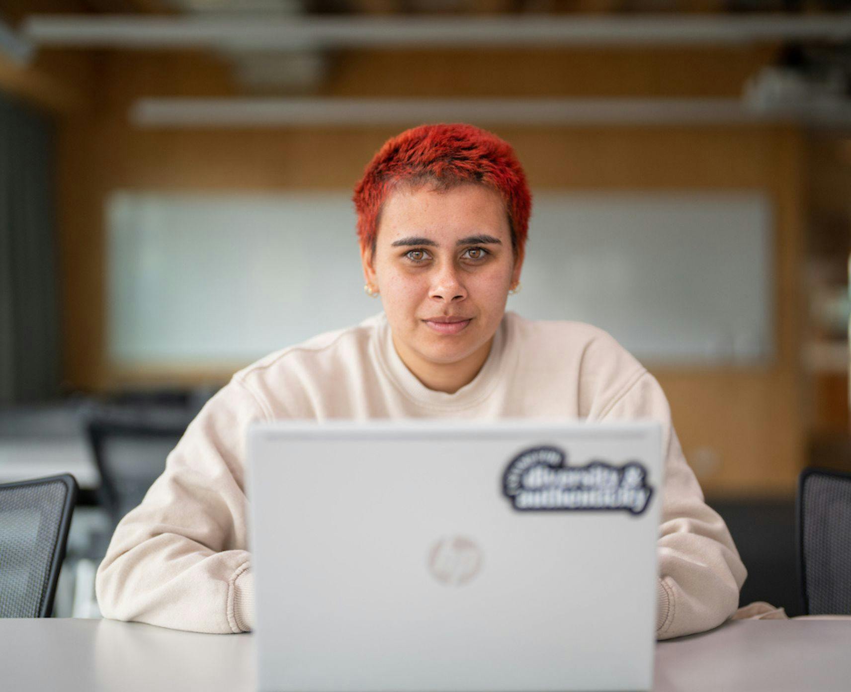 Faith Stevens sits in front of her laptop. She has cropped red hair and is wearing a beige jumper.