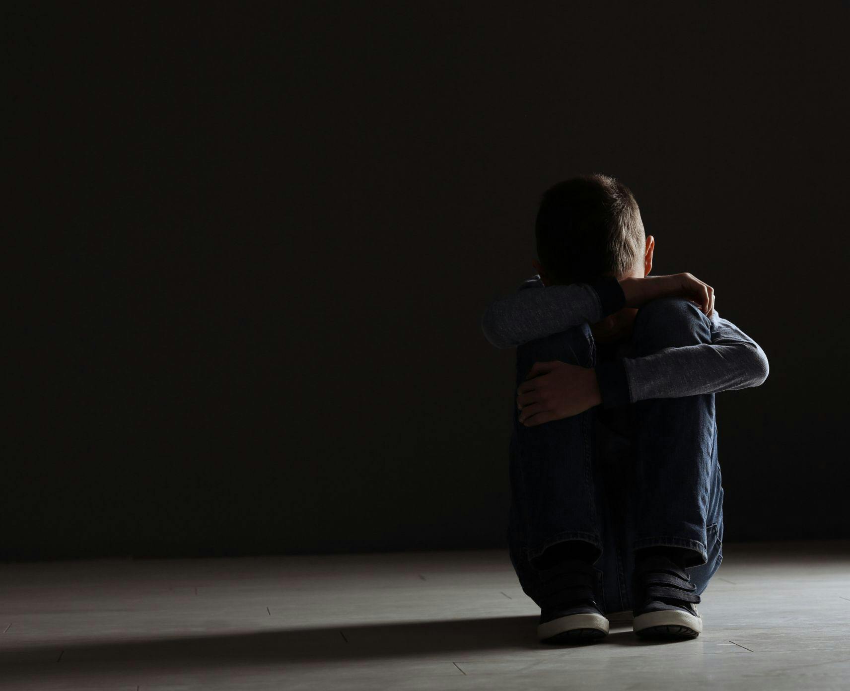 A child sits with their head down against a dark background.