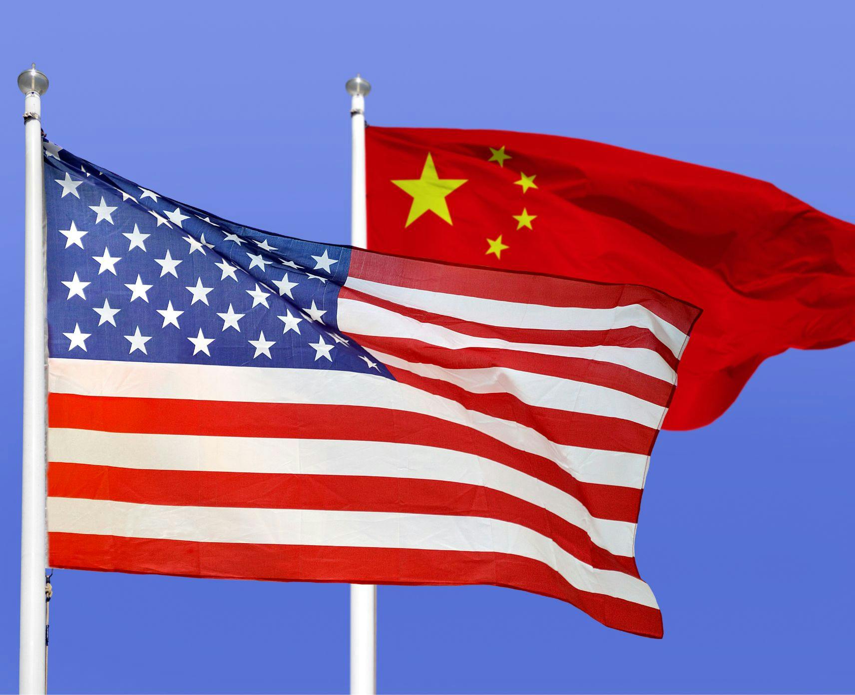 US and China flags blowing in the wind against a blue sky