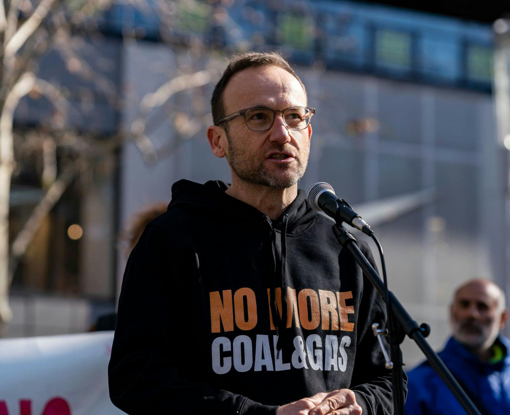 Adam Bandt in a 'No More Coal and Gas' hoddie speaking at a protest
