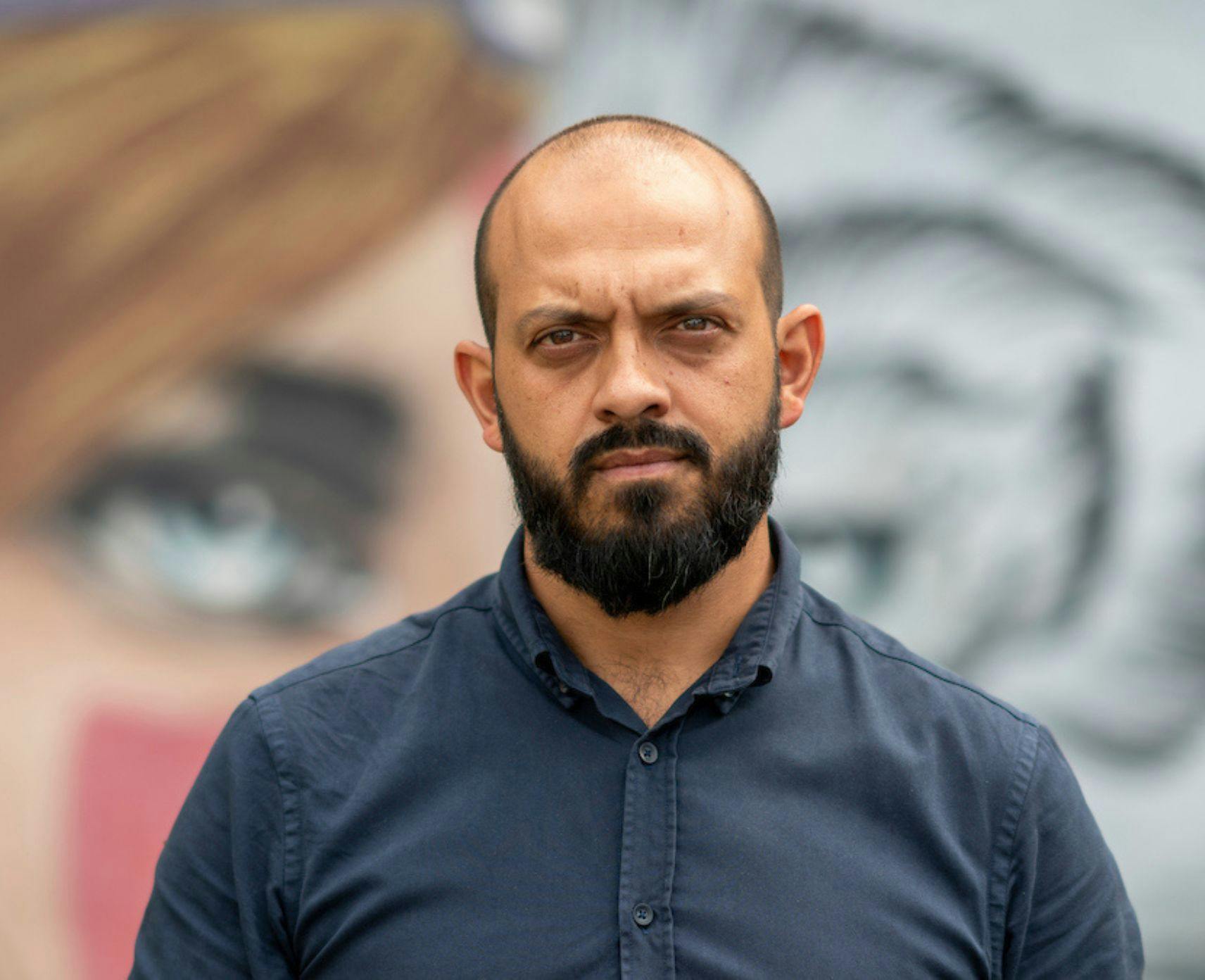 Sarouche Razi stands in front of a street art mural