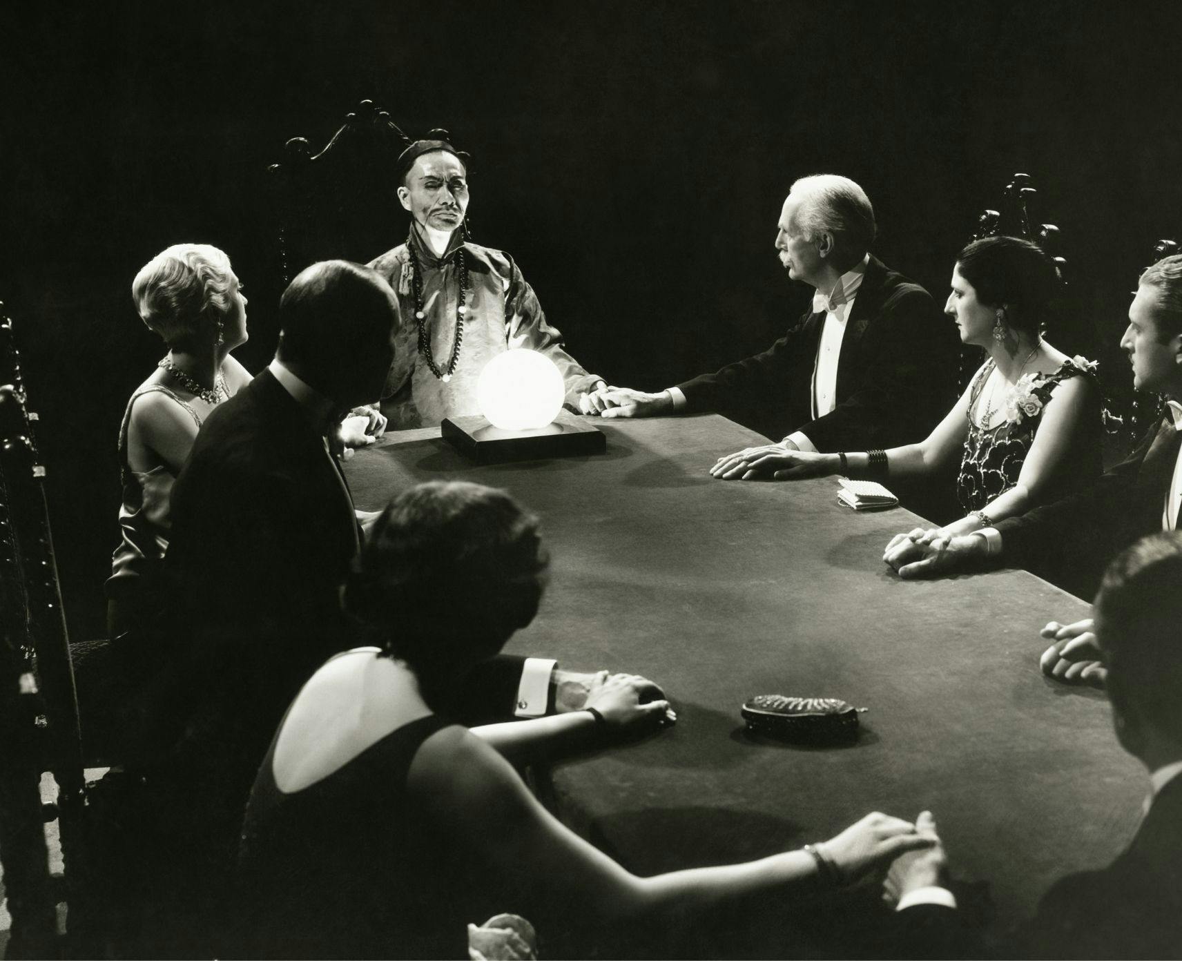 A black and white image of people sitting around a table at a seance