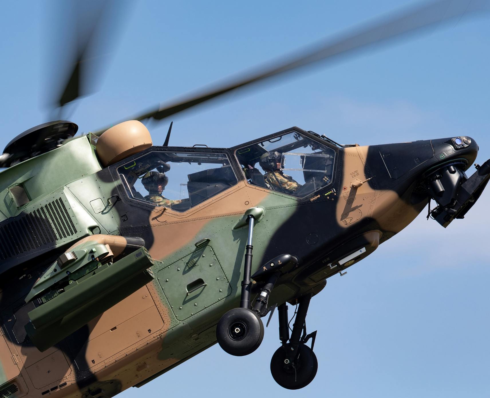 An Australian Army camouflaged helicopter flies upward against blue skies