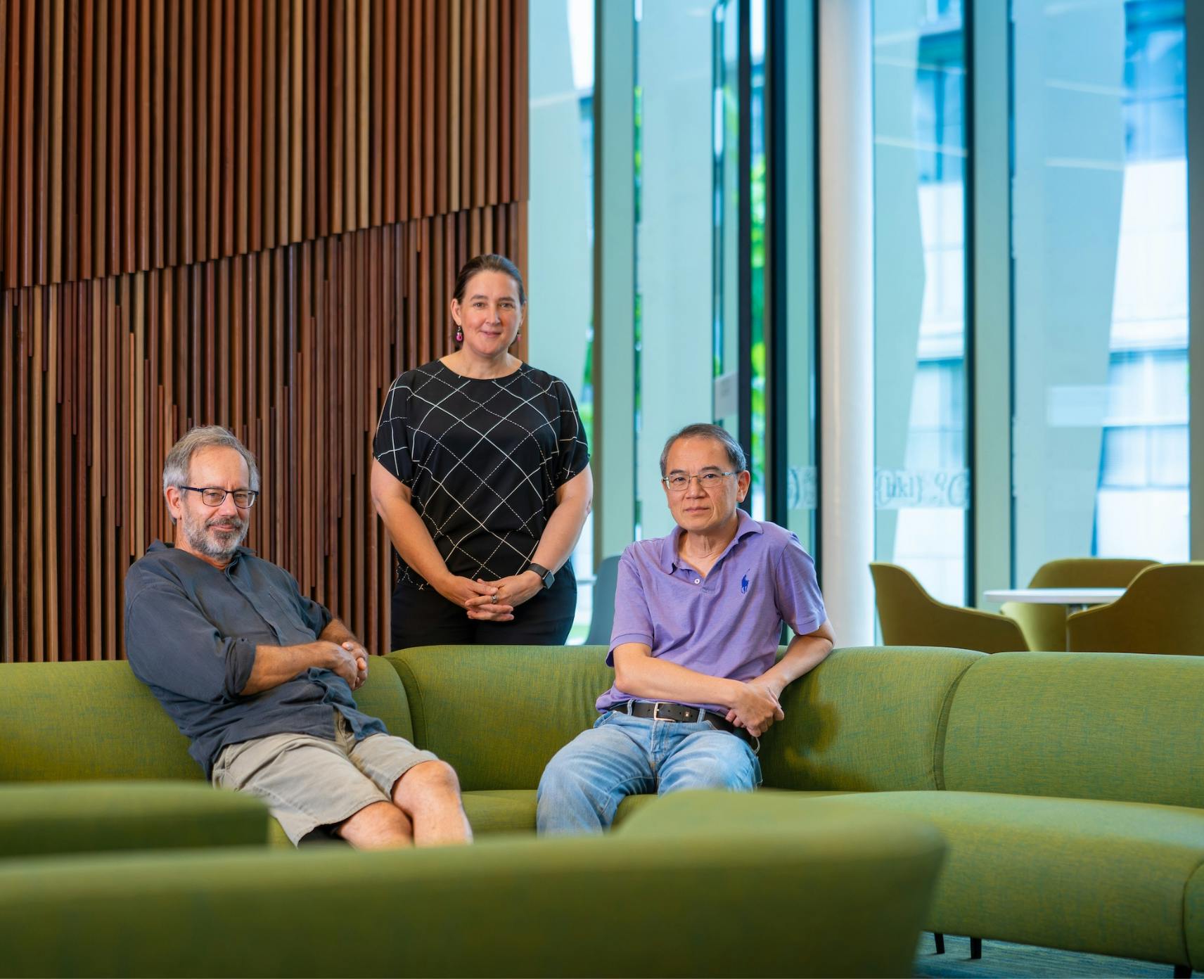 Three physicists sit on on a green couch.