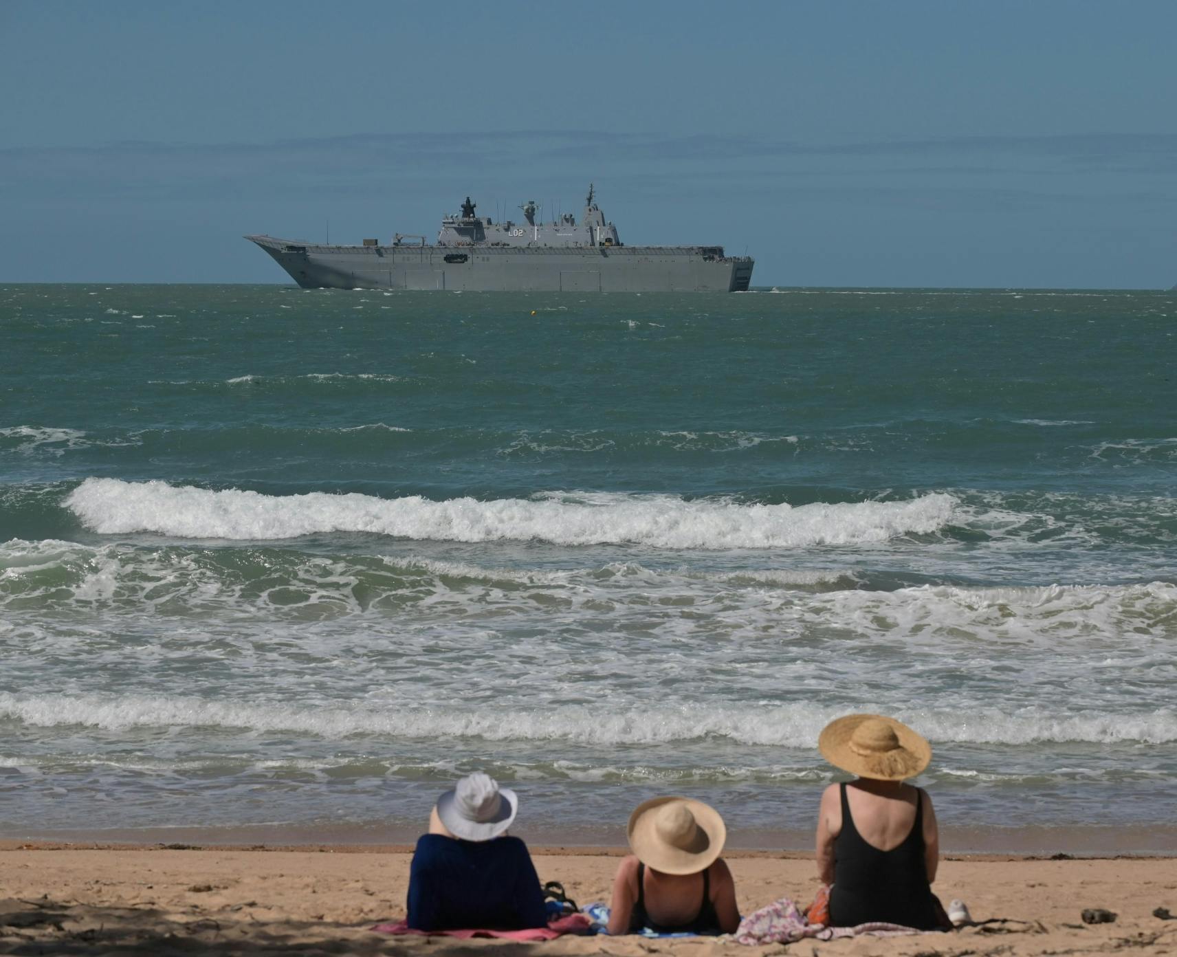 Beachgoers look at HMAS Adelaide Canberra-class landing, a Royal Australian Navy helicopter dock ship, in Townsville